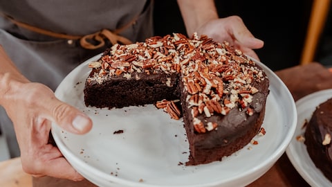 Un gâteau au chocolat et à l'avocat garni de pacanes, servi dans une assiette.