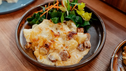 Une portion de gratin de pommes de terre, chou-fleur et merguez dans une assiette avec de la salade.