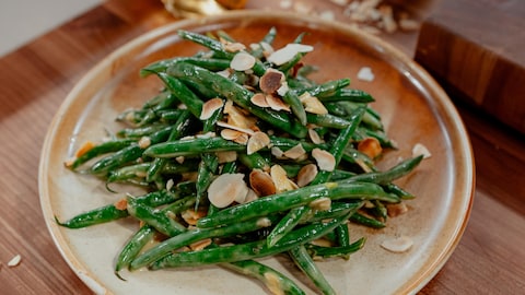 Une assiette de haricots verts garnis d'amandes rôtis et de vinaigrette.