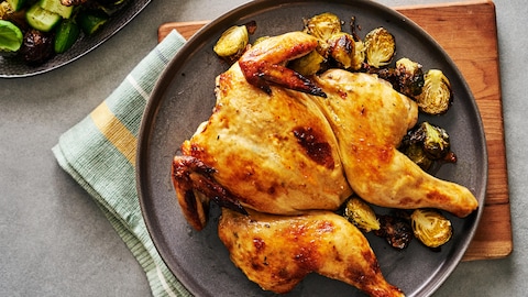Un poulet cuit en crapaudine servi avec des choux de Bruxelles rôtis.