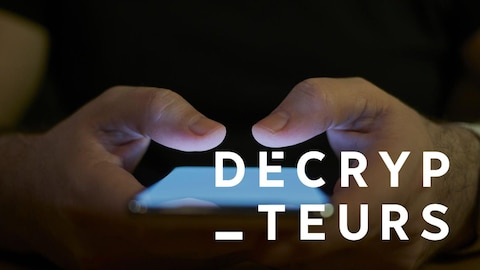 Un homme tenant entre ses mains un cellulaire allumé.