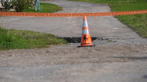 Un cône et un ruban devant le trou créé par l'affaissement de la route. 