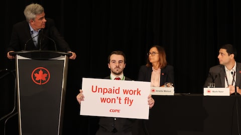 Un manifestant tient une pancarte devant des représentants d'Air Canada.