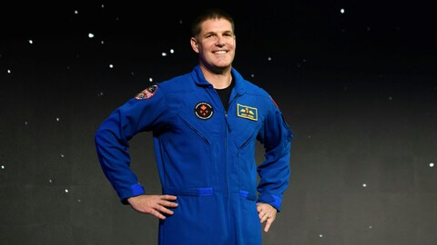 Un astronaute en combinaison de vol sourit devant la caméra. 