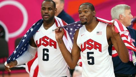 Deux basketteurs portent l'uniforme de l'équipe américaine et tiennent un drapeau de leur pays sur leurs épaules.