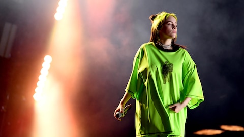 Billie Eilish porte un habit vert fluo lors d'un concert. 