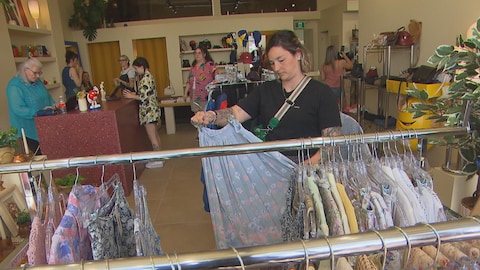 Une cliente regarde une jupe pendant que d'autres personnes magasinent dans la boutique.
