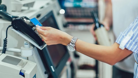 Une personne dépose une carte de paiement sur le dessus terminal de paiement à une caisse libre-service dans un commerce.