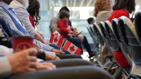 Des personnes munies de petits drapeaux canadiens, assises dans une pièce en attendant la cérémonie de citoyenneté.