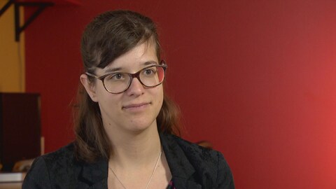 Une jeune femme est devant un mur rouge dans les bureaux de l'organisme pour lequel elle travaille. Une jeune femme est devant un mur rouge dans les bureaux de l'organisme pour lequel elle travaille.