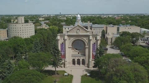 Une vue aérienne de la Carthédrale et de ses environs, qui montre l'ancienne cathédrale, qui a brûlé en 1968, et dont il ne reste que la façade de pierre. Le site est entouré d'arbres, et des édifices autour dans le quartier. Une vue aérienne de la Carthédrale et de ses environs, qui montre l'ancienne cathédrale, qui a brûlé en 1968, et dont il ne reste que la façade de pierre. Le site est entouré d'arbres, et des édifices autour dans le quartier.
