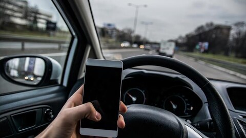 Une personne tenant un téléphone cellulaire au volant.