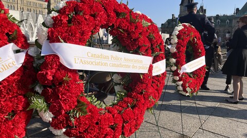 Trois couronnes de fleurs entourées chacune d'un ruban blanc avec une inscription de couleur or, placées devant le Parlement. Sur celle du centre, il est écrit « L'Association canadienne des policiers ».
