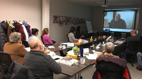 On voit des participants autour d'une table qui regardent sur un écran une simulation d'entrevue enregistrée, en vue de la commenter.