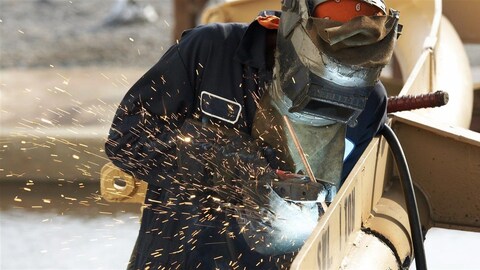 Un travailleur utilise une pince dans une main et de l'autre une soudeuse. Il travaille à joindre deux pièces ensemble. 