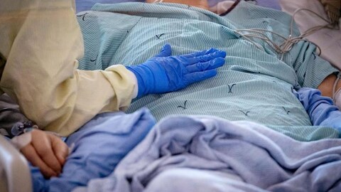 Une personne avec des gants sanitaires pose sa main sur la poitrine d'une personne âgée couchée dans un lit d'hôpital.