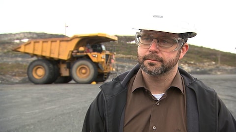 David Cataford avec un casque de construction. En arrière-plan, un camion lourd. David Cataford avec un casque de construction. En arrière-plan, un camion lourd.