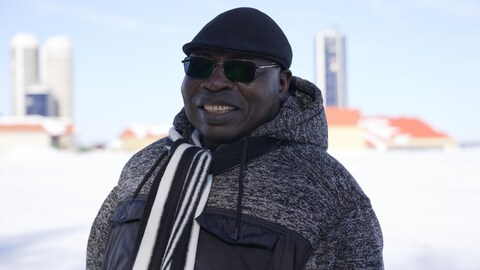 Un homme d'origine africaine avec son manteau d'hiver et son foulard tout sourire à l'extérieur.