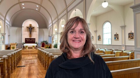 Une femme debout à l'intérieur de l'église, dans l'allée centrale.