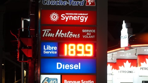 Un panneau publicitaire éclairé, la nuit, dans une station-service, affichant le litre d'ordinaire à 1,89 $.