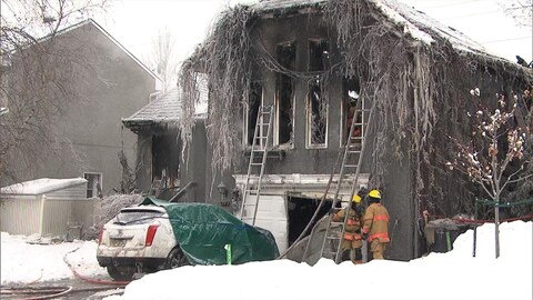 Des pompiers devant une maison calcinée.
