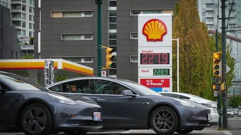 Three Tesla electric vehicles drive past a sign displaying the price of gas in Vancouver on May 14, as it reached a new high of $2.28 a litre. Despite a drop in inflation for July, for Tesla drivers and others who don't use gas, prices are still climbing. (Darryl Dyck/The Canadian Press)