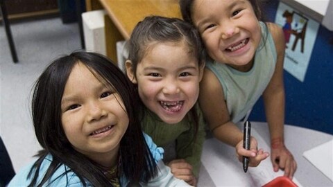 ثلاثة أطفال من سكان كندا الأصليين في قاعة مدرسة.