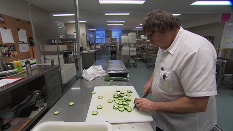 Un cuisinier coupe des concombres.