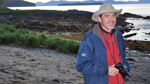Un homme avec un chapeau tient un appareil photo, en arrière-plan on voit la nature. Un homme avec un chapeau tient un appareil photo, en arrière-plan on voit la nature.