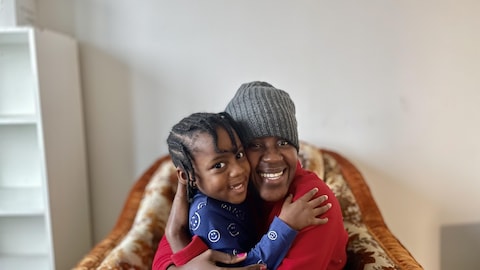 Tania Henriques, assise sur son fauteuil, fait un câlin à sa fille. Les deux regardent l'appareil photo, le sourire aux lèvres.