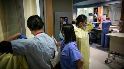 Nurses putting on gowns in a hospital ward.