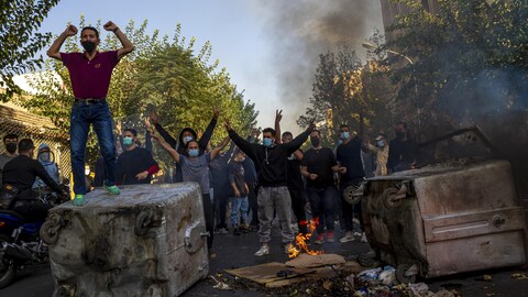 Des hommes lèvent les bras en l'air près d'une barricade établie dans une rue.