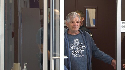 Jean-Marc Beaudin, accompagné de policiers, sort d'un bâtiment.