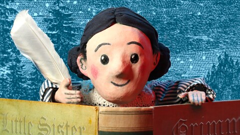Une marionnette représentant une petite fille qui tient une plume et un livre.