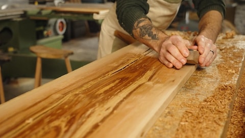 Radio-Canada Un homme plane une planche de bois.