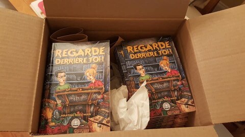Plusieurs exemplaires de « Regarde derrière toi! » dans une boîte. Plusieurs exemplaires de « Regarde derrière toi! » dans une boîte.