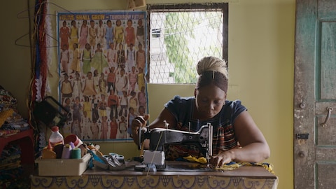 Une femme africaine coud un tissu à la machine à coudre.
