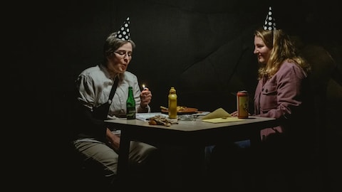 Deux personnes assises autour d'une table, un chapeau en forme de cone sur la tête.