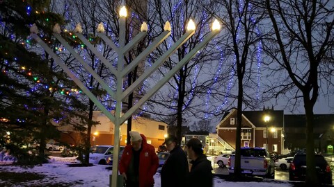Trois personnes devant un lampadaire en forme de chandelier à neuf branches.