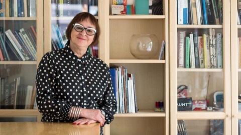 Une photo de Monique Savoie devant une grande bibliothèque en bois.