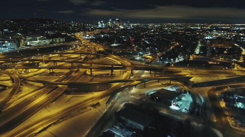 Une vue aérienne et de nuit de l'échangeur Turcot, avec au fond le centre-ville de Montréal.