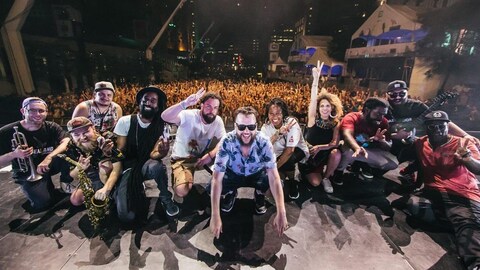Le groupe Nomadic Massive prend fièrement la pose sur la grande scène du Festival de jazz de Montréal, avec la foule en arrière-plan. 