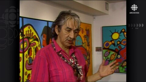 Norval Morrisseau et tableaux en arrière-plan. 