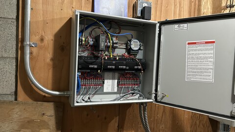 Un boîtier ouvert posé au mur, dans lequel il y a beaucoup de fils et de branchements.