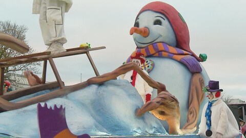 Des gens costumés en bonhomme de neige sont sur un char allégorique où se trouve un immense bonhomme de neige et un traîneau. 