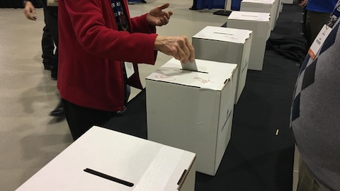 Une dame glisse une enveloppe dans une urne pour voter.