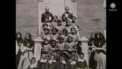 Photo de groupe d'enfants autochtones, avec des religieux et des sœurs autour d'eux.