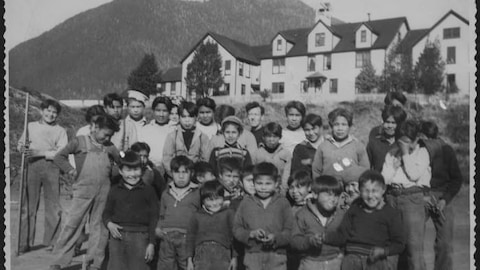 La photo d'archives en noir et blanc montre un groupe d'enfants qui posent dehors. 