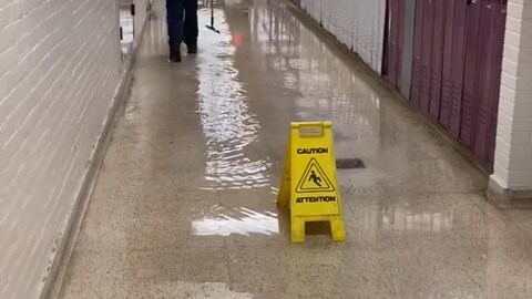 Une affiche posée sur le plancher inondé dit : « attention ».