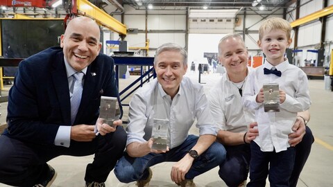 Trois hommes accompagnés d'un jeune garçons posent fièrement dans une usine de fabrication de structures d'acier.               